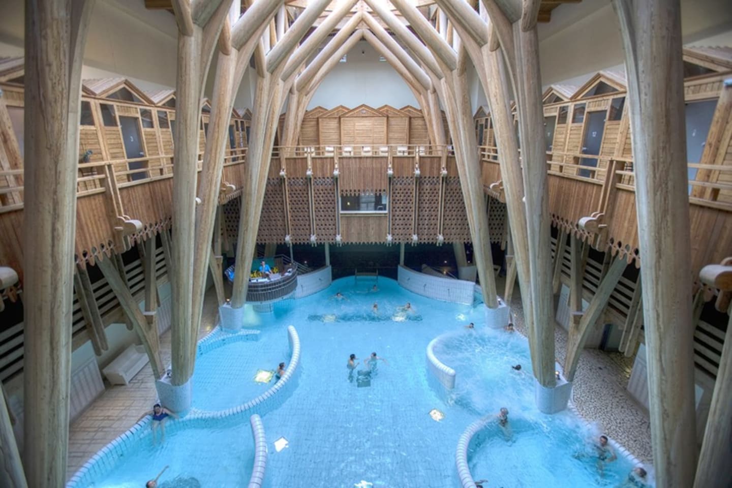 Indoor aquatic center at Les Chalets Du Lac De Montréjeau with blue pools, wooden beam architecture, and changing cabins.