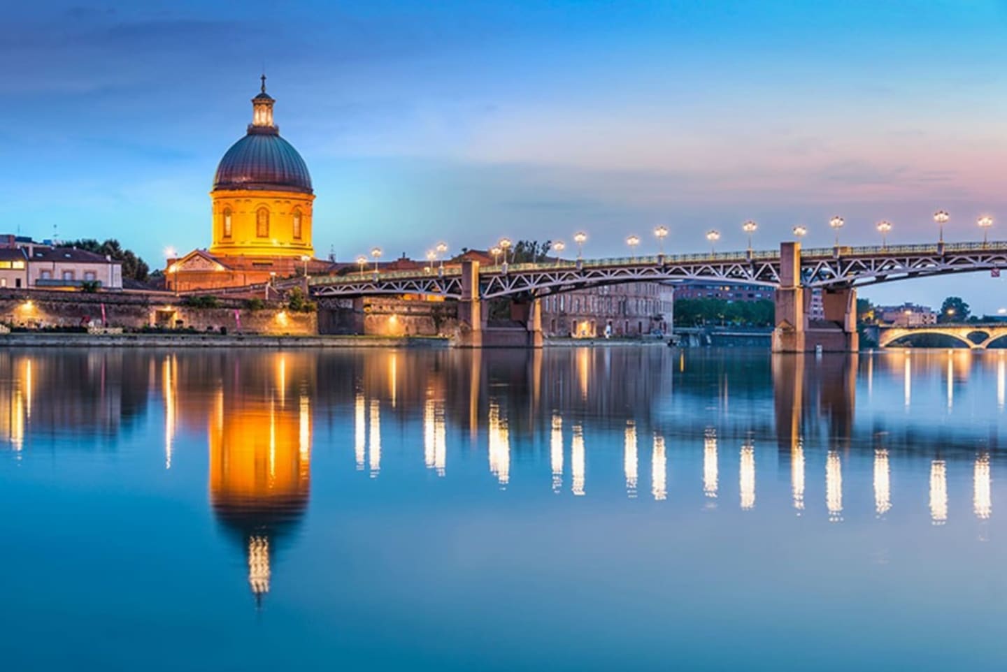 Dôme doré illuminé et pont de fer se reflétant dans l'eau bleue calme au crépuscule près de Clarac, France