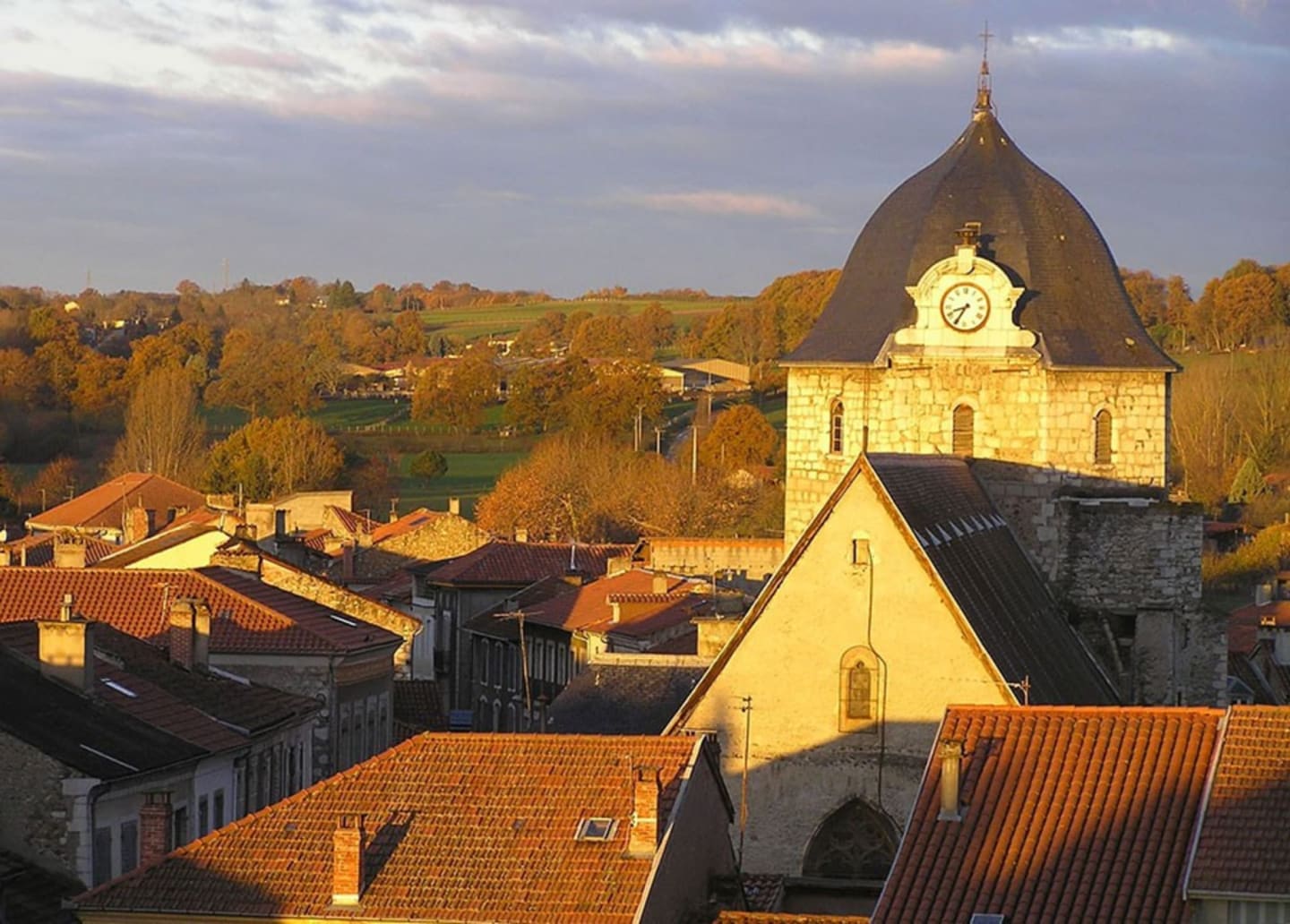 Iglesia histórica con campanario de cúpula en Clarac, Francia, rodeada de árboles otoñales y edificios tradicionales