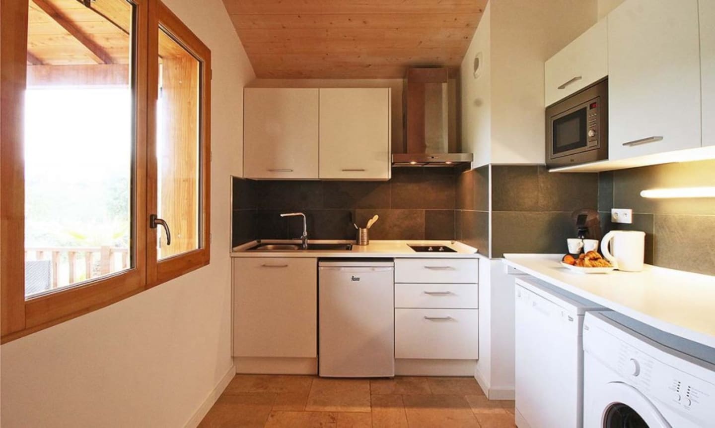 Cuisine moderne aux armoires blanches, dosseret foncé et plafond en bois aux Chalets Du Lac De Montréjeau