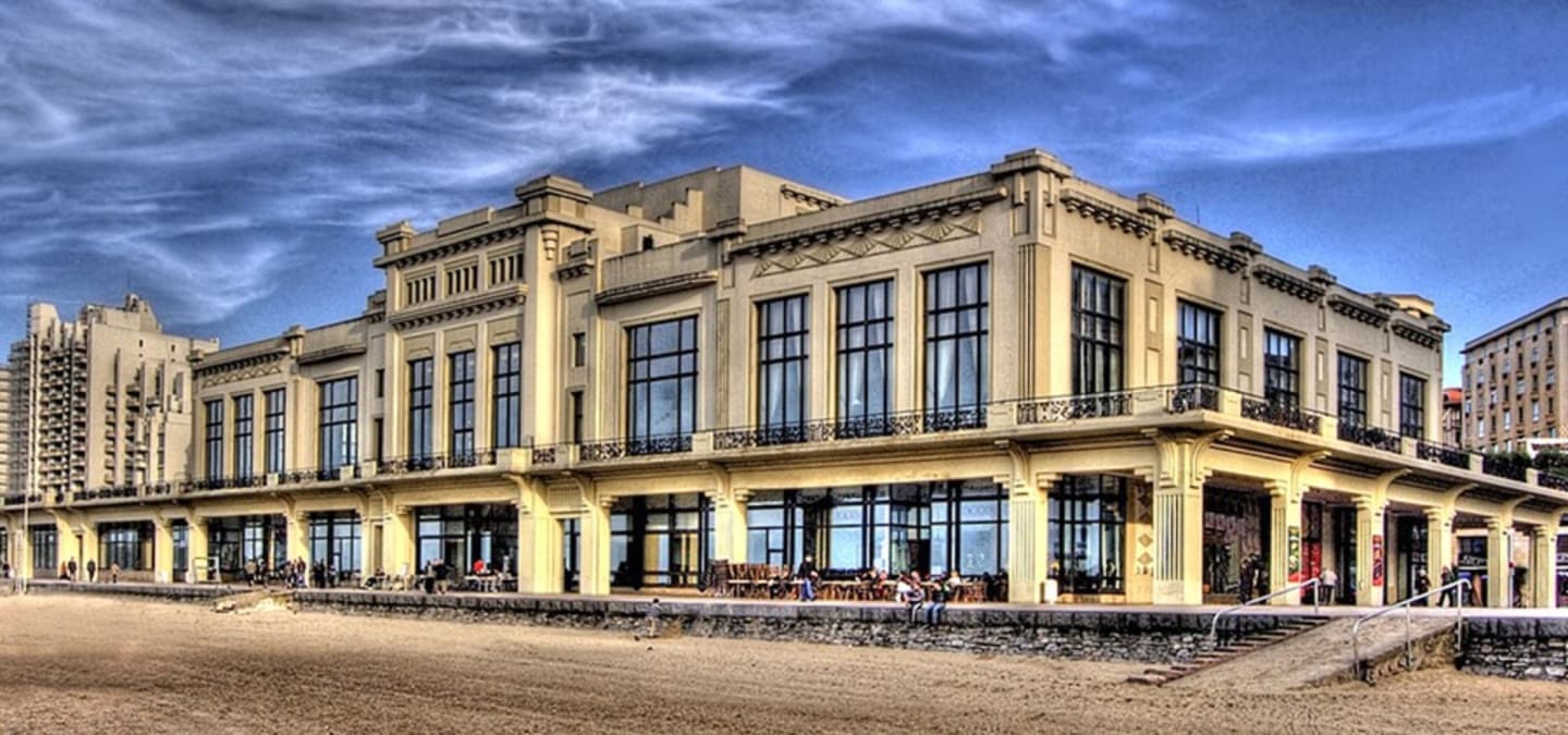 Edificio Belle Époque frente al mar con fachada crema y oro, grandes ventanales y columnata en planta baja en Clarac, Francia