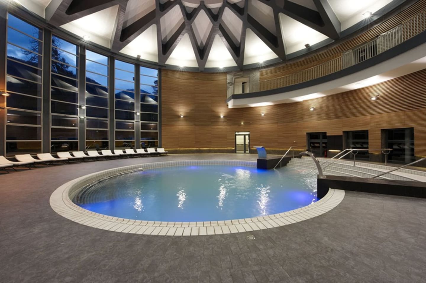 Modern indoor swimming pool at Les Chalets Du Lac with blue-lit water, wooden walls, and lounge chairs in Clarac, France