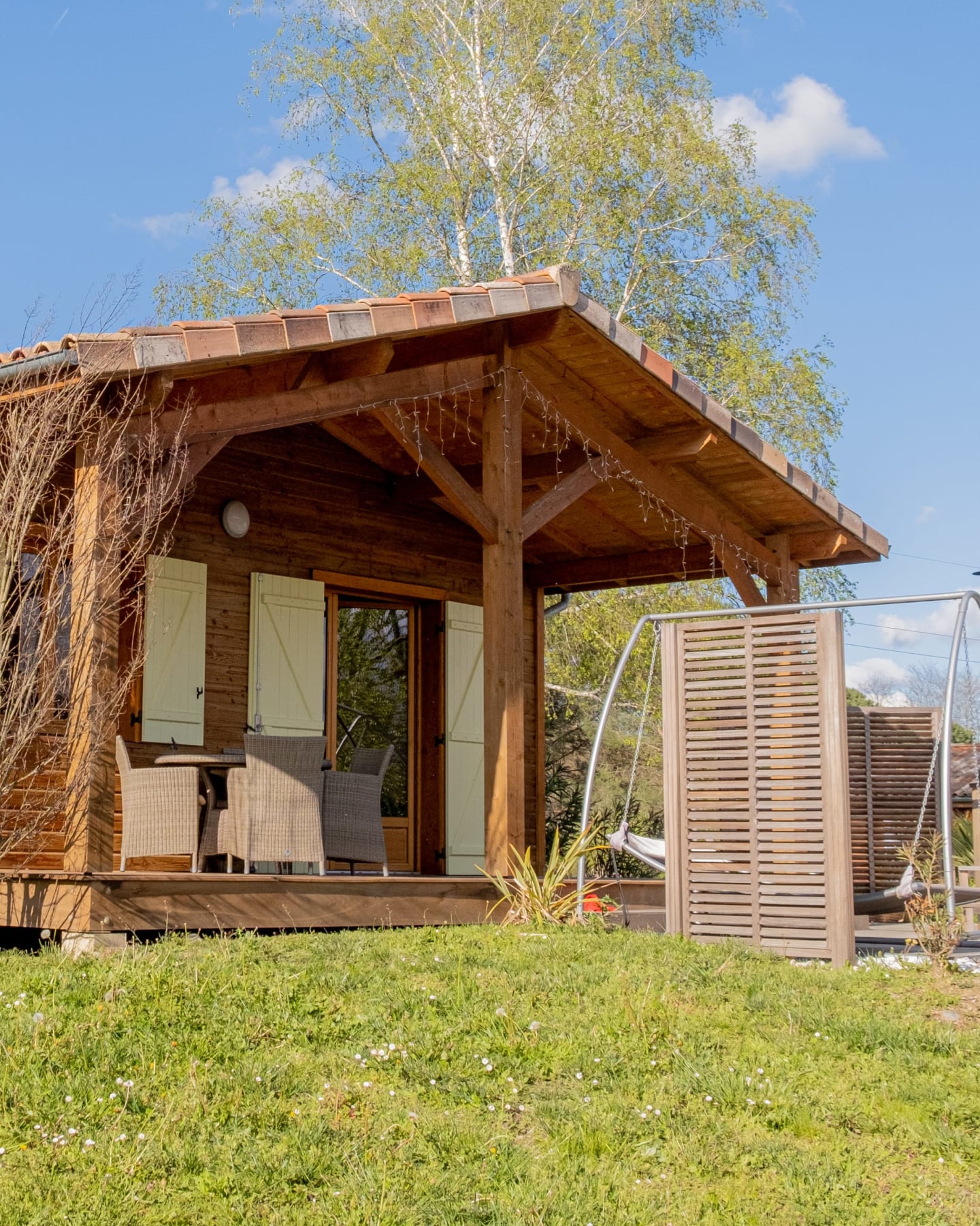 Chalet en bois avec patio couvert aux Chalets Du Lac De Montréjeau, Clarac, entouré de pelouse verte et de bouleaux