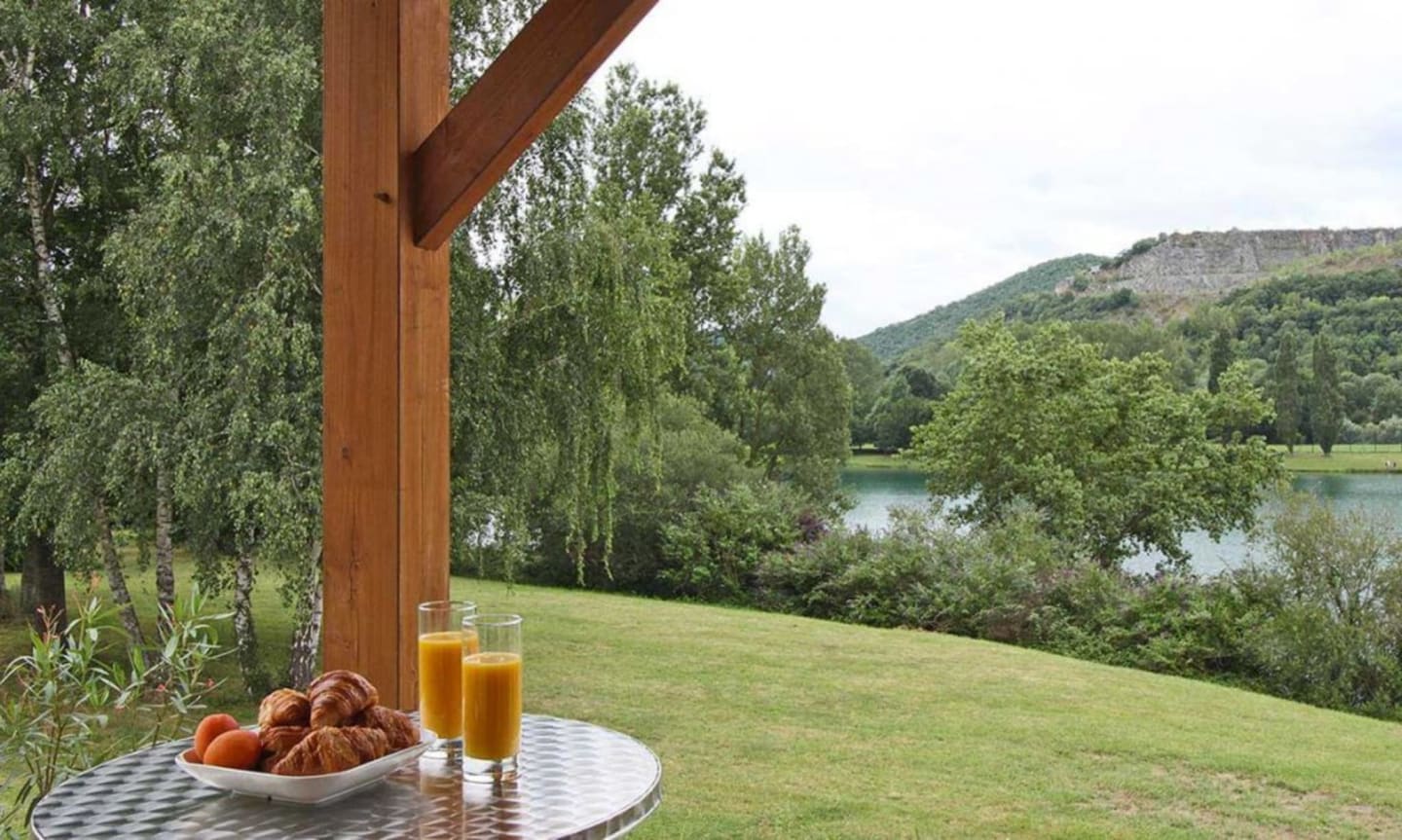 Terrasse extérieure des Chalets Du Lac avec croissants, jus d'orange et vue panoramique sur le lac et les montagnes à Clarac, France