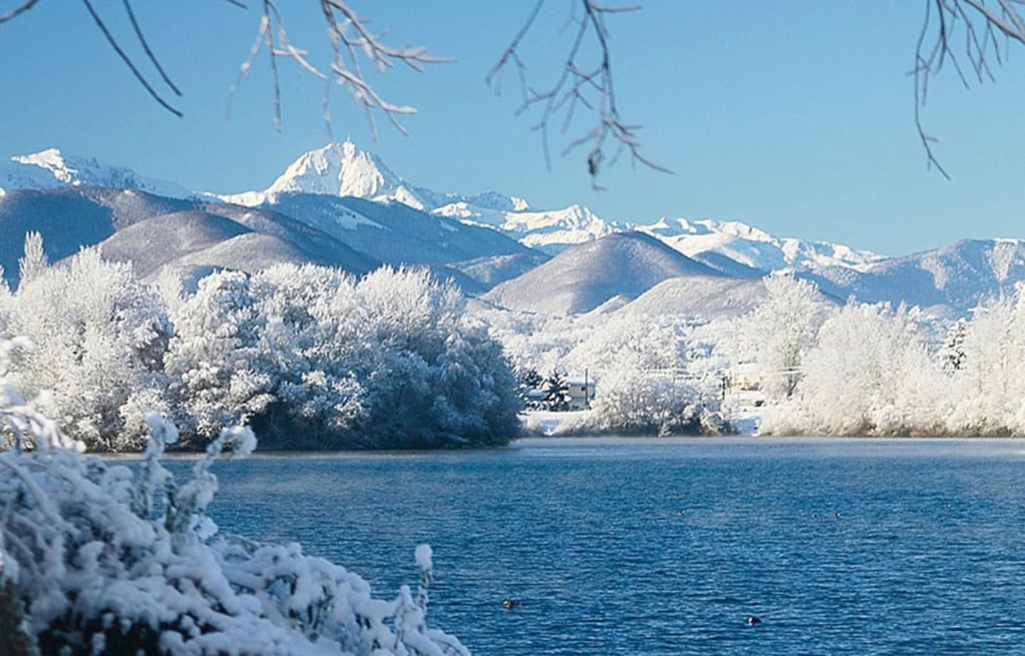 Des arbres givrés et des montagnes enneigées encadrent un lac bleu cristallin aux Chalets Du Lac, Clarac.