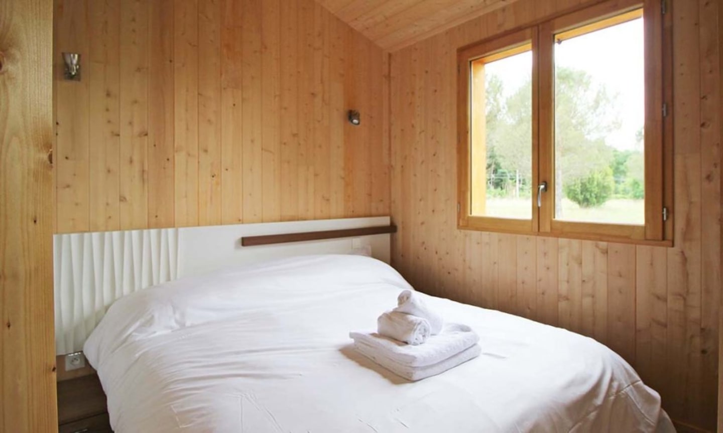 Chambre douillette en bois aux Chalets Du Lac De Montréjeau avec literie blanche, serviettes roulées et grandes fenêtres avec vue