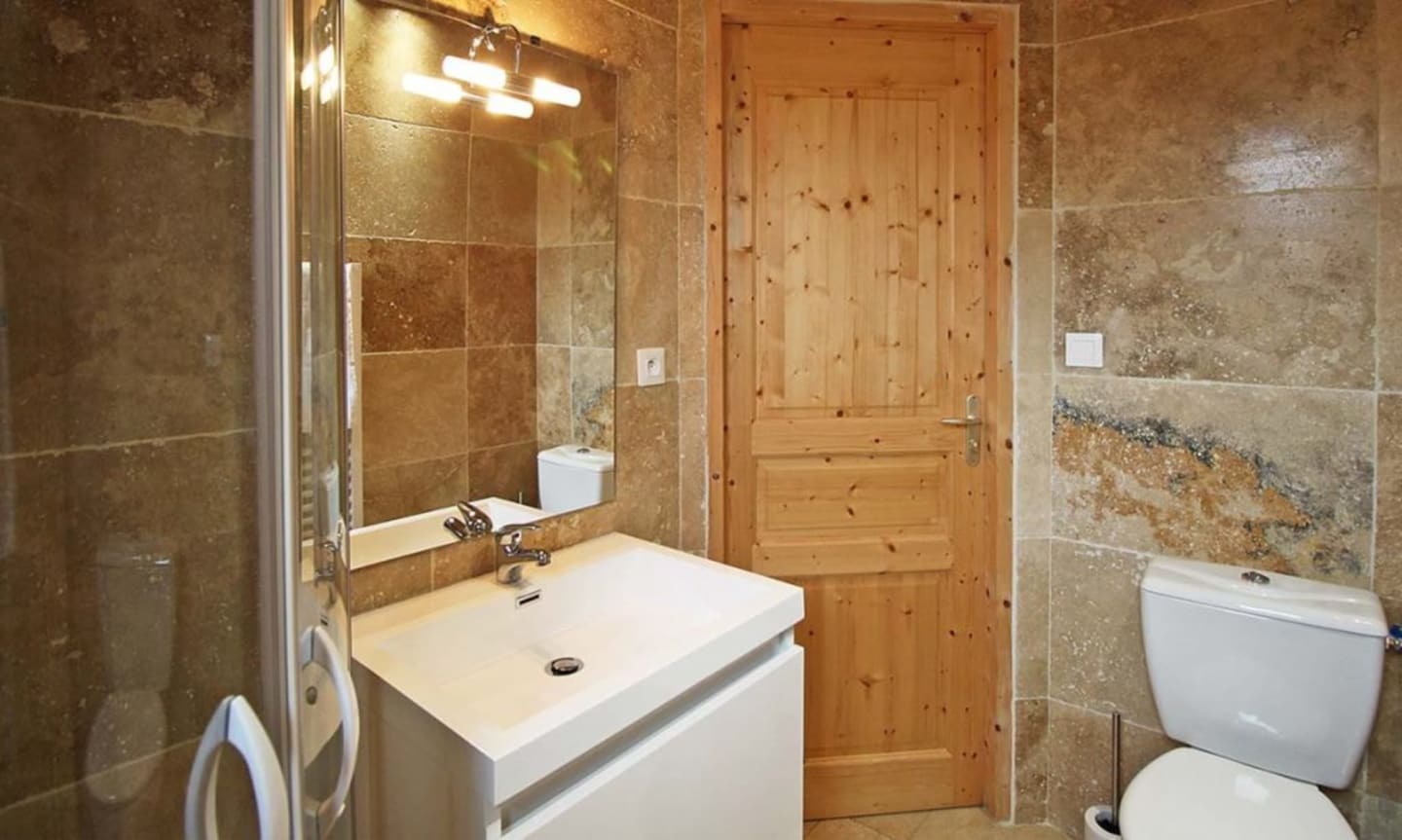 Salle de bains aux Chalets Du Lac De Montréjeau avec lavabo blanc, carrelage marron, porte en bois et toilettes à Clarac