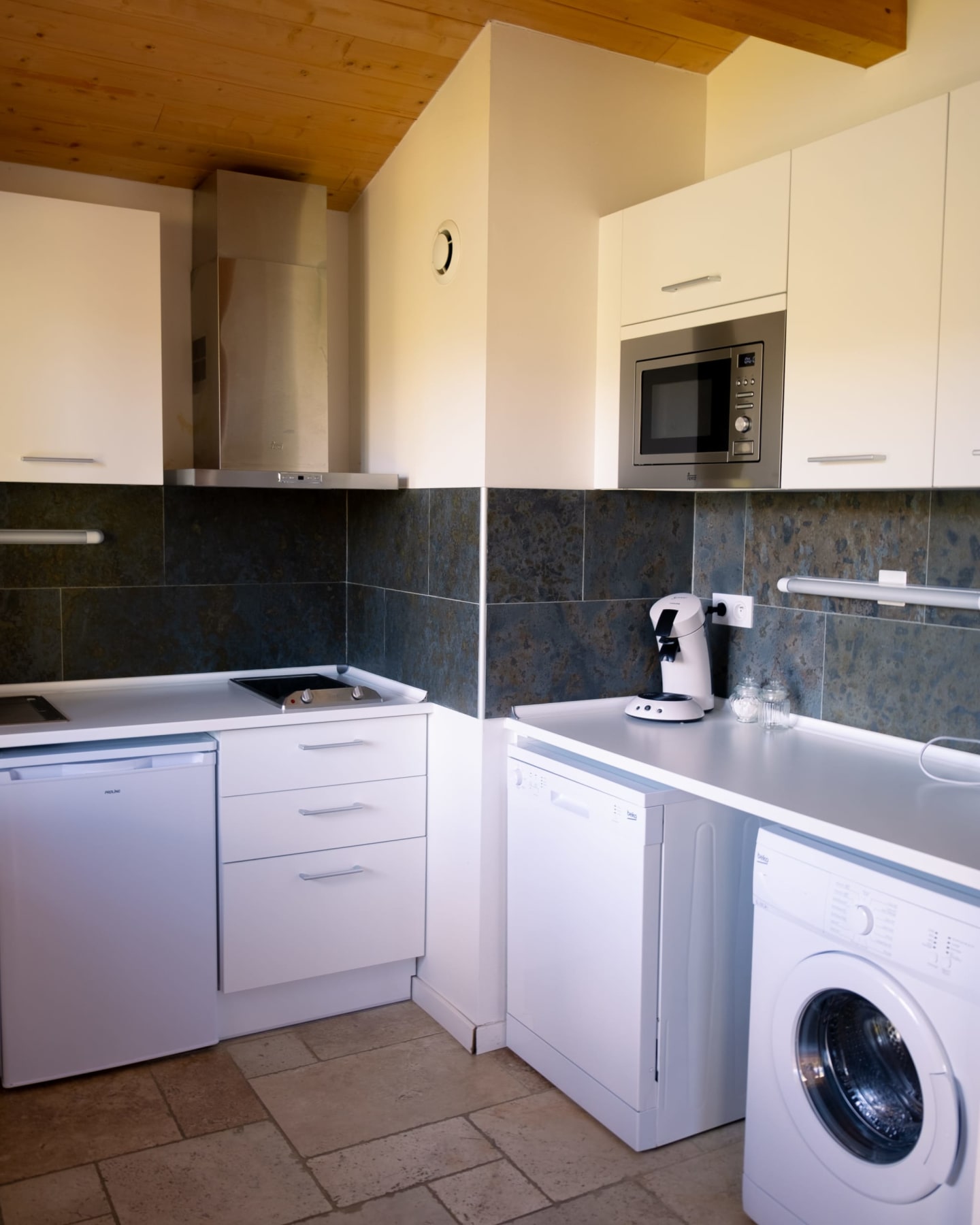 Cuisine moderne aux armoires blanches, dosseret en carrelage foncé, électroménagers inox et lave-linge aux Chalets Du Lac De