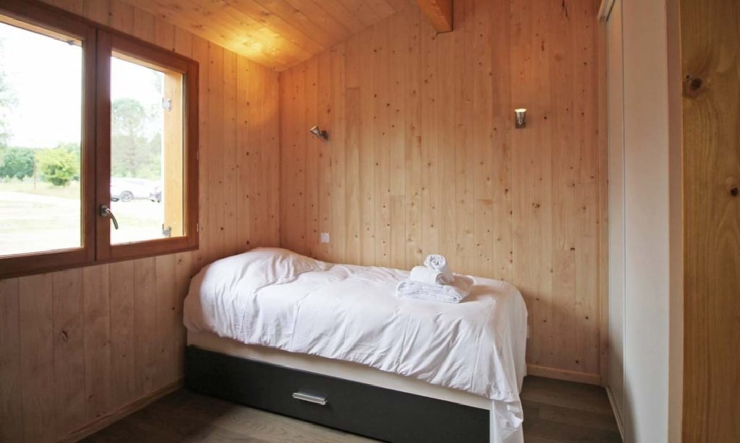 Chambre chaleureuse en bois au chalet Les Chalets Du Lac De Montréjeau, Clarac avec lit simple aux draps blancs et fenêtre