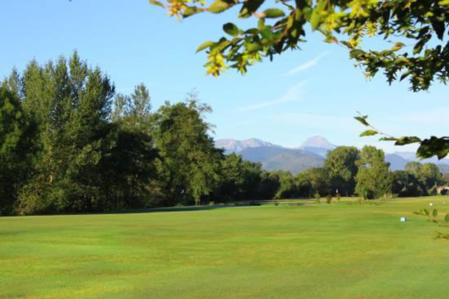 Superbe terrain de golf verdoyant aux Chalets du Lac avec fairways bordés d'arbres et montagnes en arrière-plan à Clarac