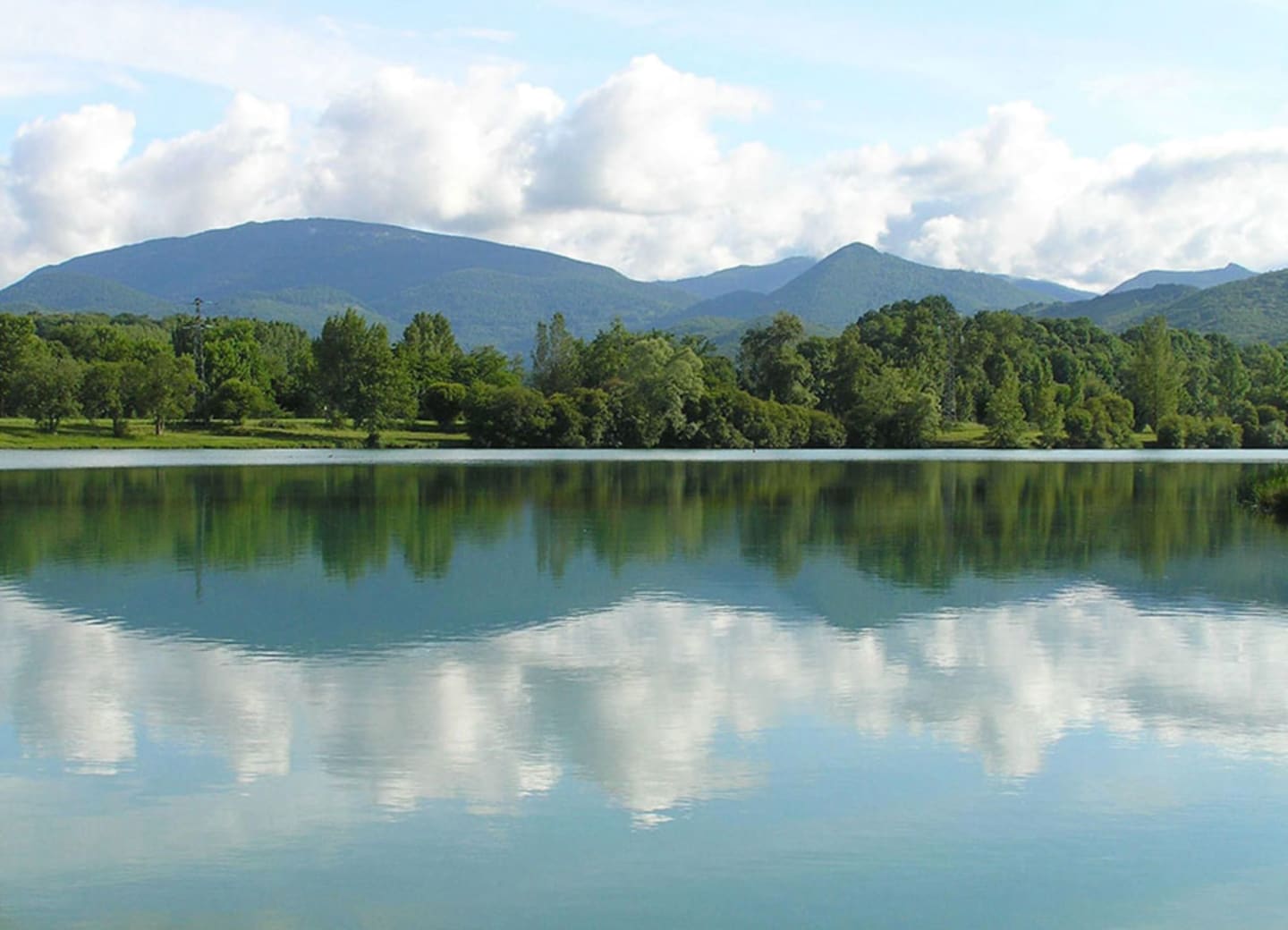 Vue sereine sur le lac avec rives boisées et pics montagneux se reflétant dans les eaux calmes aux Chalets Du Lac De Montréjeau, Clarac