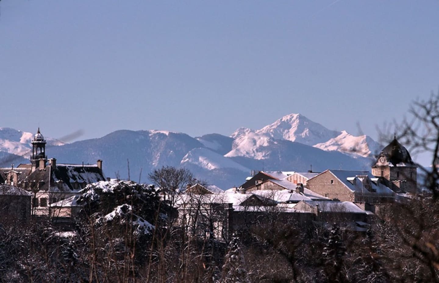 Pueblo alpino cubierto de nieve con picos montañosos y campanarios de iglesia en Clarac, Pirineos franceses