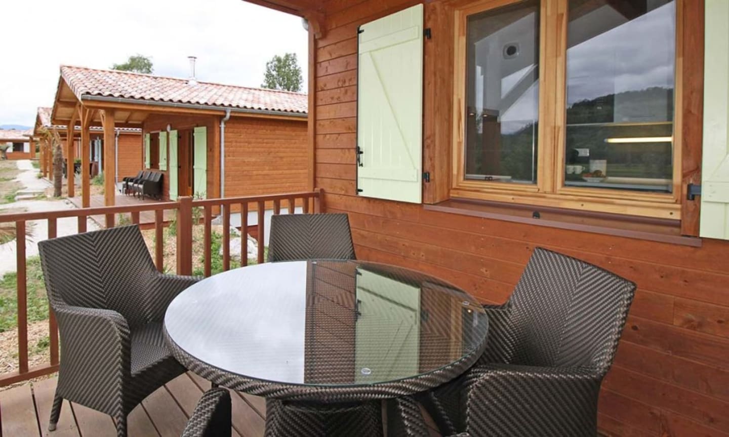 Terrasse extérieure des Chalets Du Lac avec chaises tissées et table ronde face au lodge en bois à Clarac