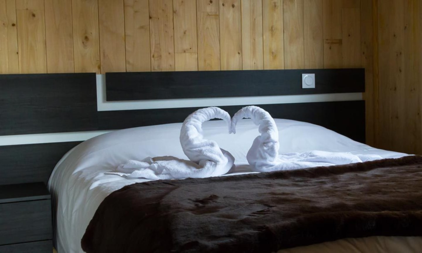 Cygnes en serviettes sur le lit avec chemin de table foncé aux Chalets Du Lac De Montréjeau, Clarac