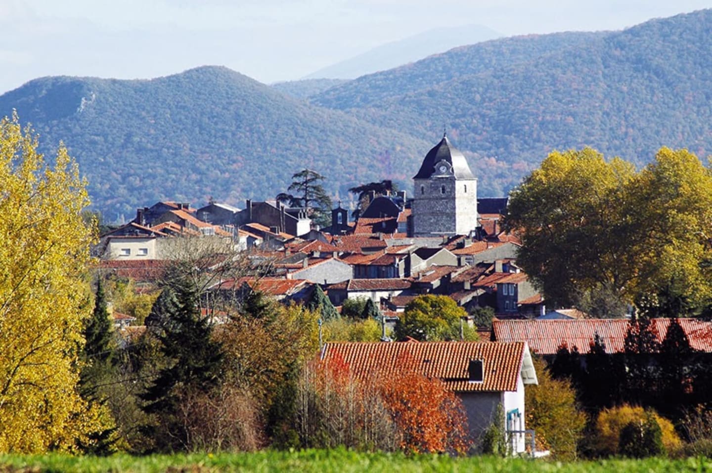 Encantador pueblo medieval de Clarac con torre iglesia, tejados de tejas rojas y montañas boscosas de fondo cerca de Les Chalets Du Lac
