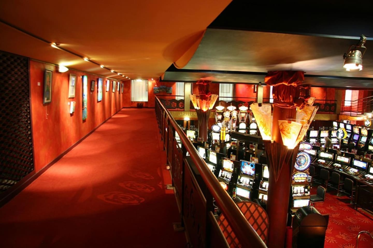 Sala de juegos del casino con alfombra roja, máquinas tragaperras e iluminación ornamental en Les Chalets Du Lac
