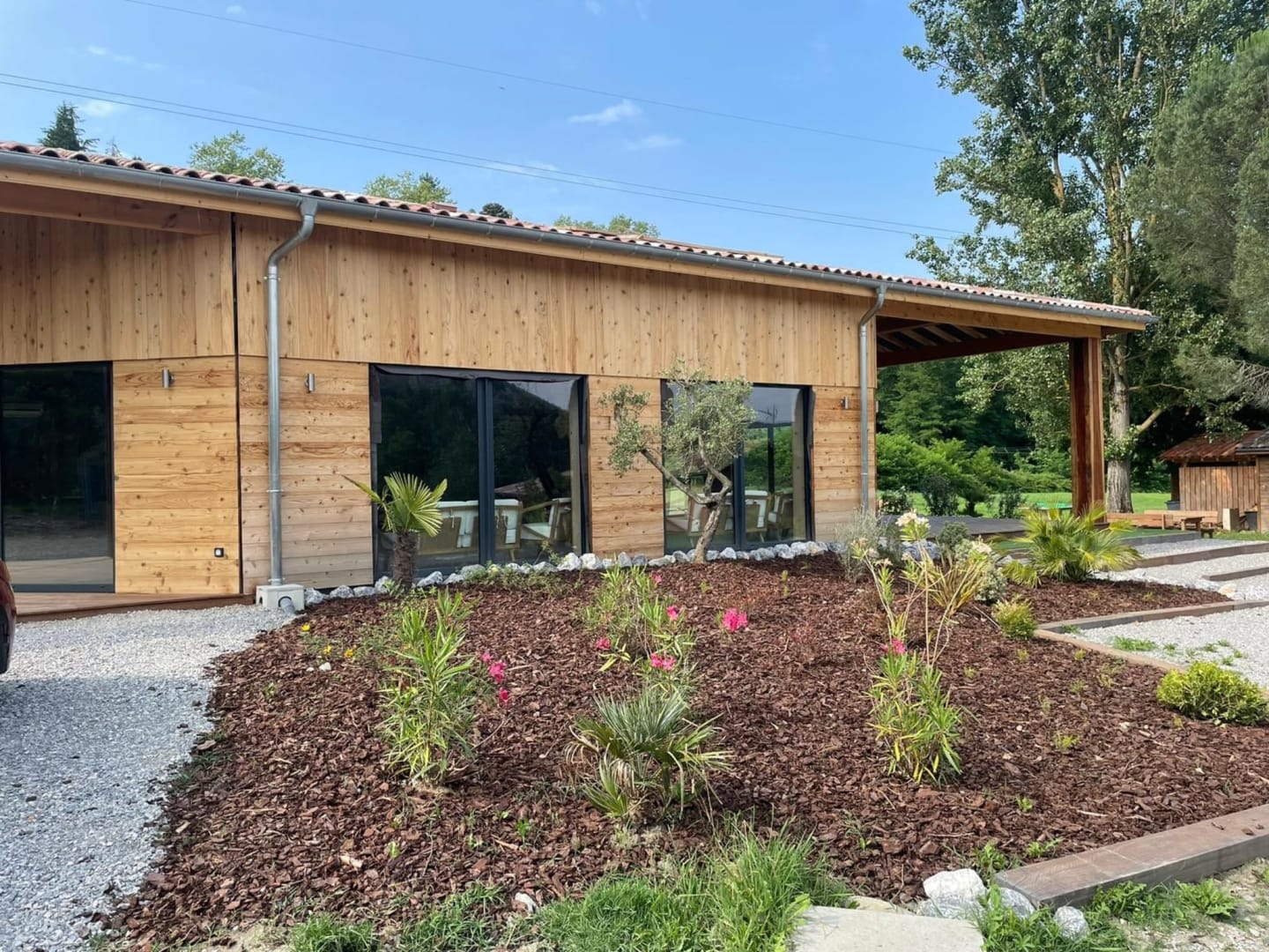 Extérieur de la salle d'événementiel en bois de l'hôtel des Chalets de Montréjeau avec sa verdure environnante.