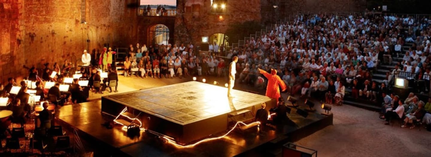 Grand événement théâtral avec orchestre et artistes sur scène illuminée devant un public nombreux dans un lieu historique