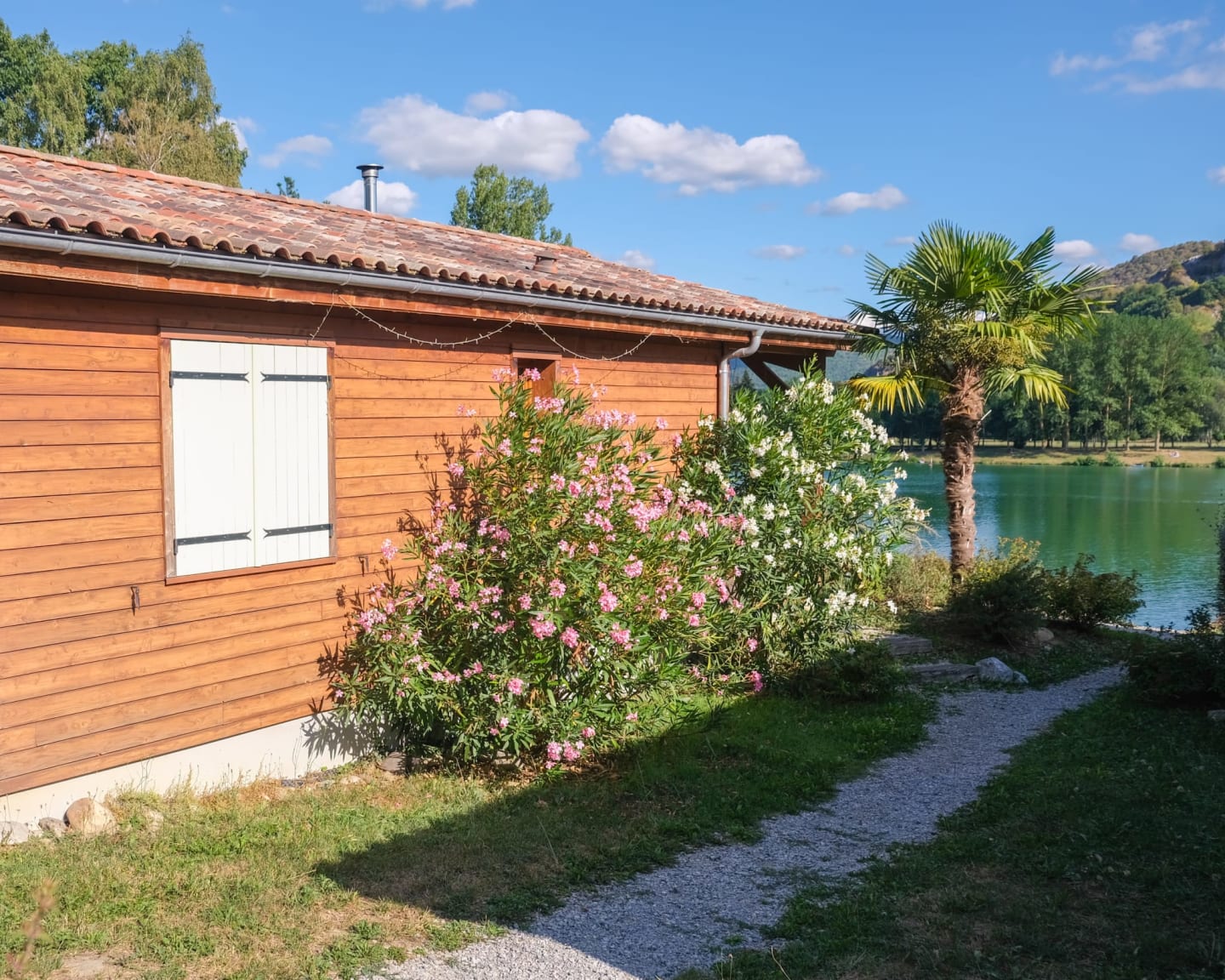 Chalet en bois avec fleurs roses et palmier dominant le lac aux Chalets Du Lac De Montréjeau