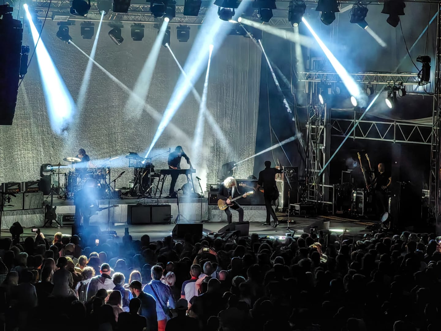 Concert en direct avec groupe sur scène, éclairages bleus dramatiques et public nombreux aux Chalets du Lac de