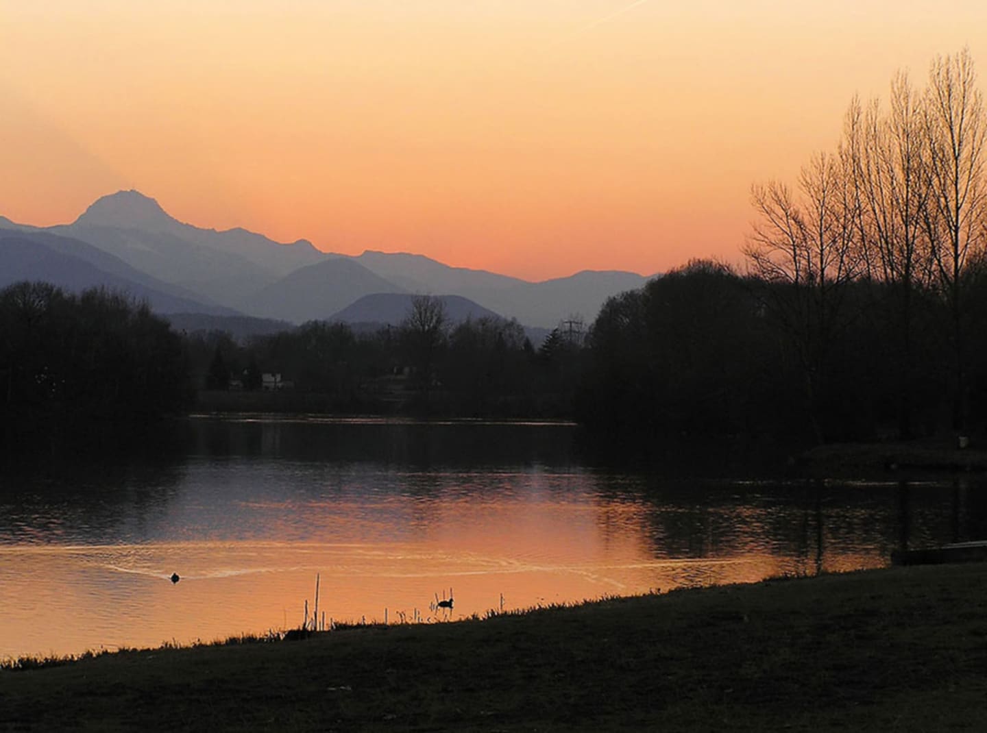 Coucher de soleil sur le lac avec montagnes et arbres nus aux Chalets Du Lac, Montréjeau Clarac France